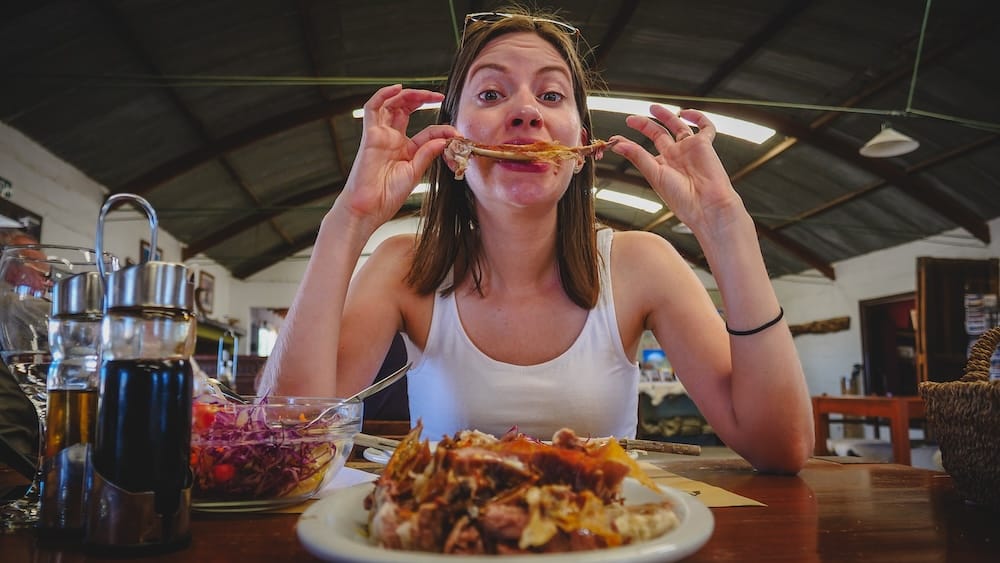 Audrey Bergner eating Patagonian lamb ribs by hand at Estancia San Lorenzo in Península Valdés Argentina, highlighting cordero al asador experience, bone-in cuts, rustic dining, and hands-on gaucho-style eating typical of Patagonian lamb meals