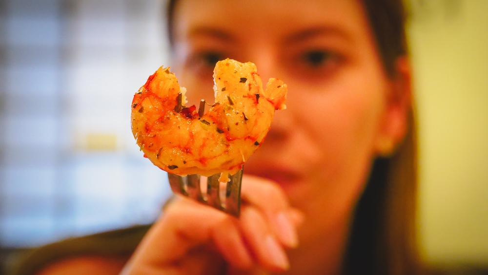 Patagonian grilled shrimp seafood in Península Valdés Argentina with Audrey Bergner Península Valdés Patagonian seafood close-up where Audrey Bergner holds grilled shrimp on a fork highlighting the fresh Atlantic coastal cuisine travelers discover while exploring Argentina’s famous wildlife reserve and coastal route.