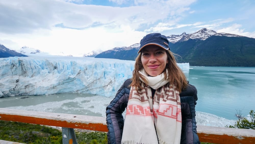 Perito Moreno Glacier Viewpoint Near El Calafate, Patagonia, Argentina, with Audrey Bergner Audrey Bergner stands at a wooden viewpoint above Perito Moreno Glacier near El Calafate, Santa Cruz, Patagonia, Argentina, with blue ice, turquoise water and snow-capped mountains behind her.