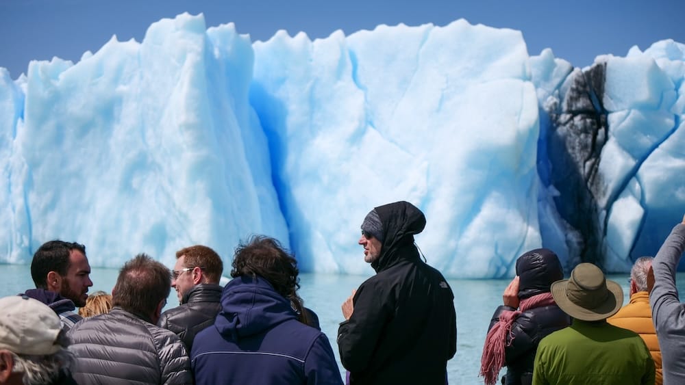 Tourists in warm jackets observe the towering blue ice wall of Perito Moreno Glacier from a boat on Lago Argentino near El Calafate, Santa Cruz, Patagonia, Argentina.