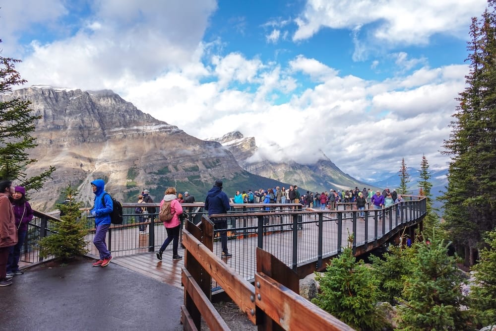 Plataforma de observación de Bow Summit en el lago Peyto, Icefields Parkway — Parque Nacional Banff, Alberta Visitantes caminando por la plataforma de observación pavimentada en el mirador de Bow Summit/lago Peyto en la Icefields Parkway, montañas y nubes de fondo, Parque Nacional Banff, Alberta, Canadá.