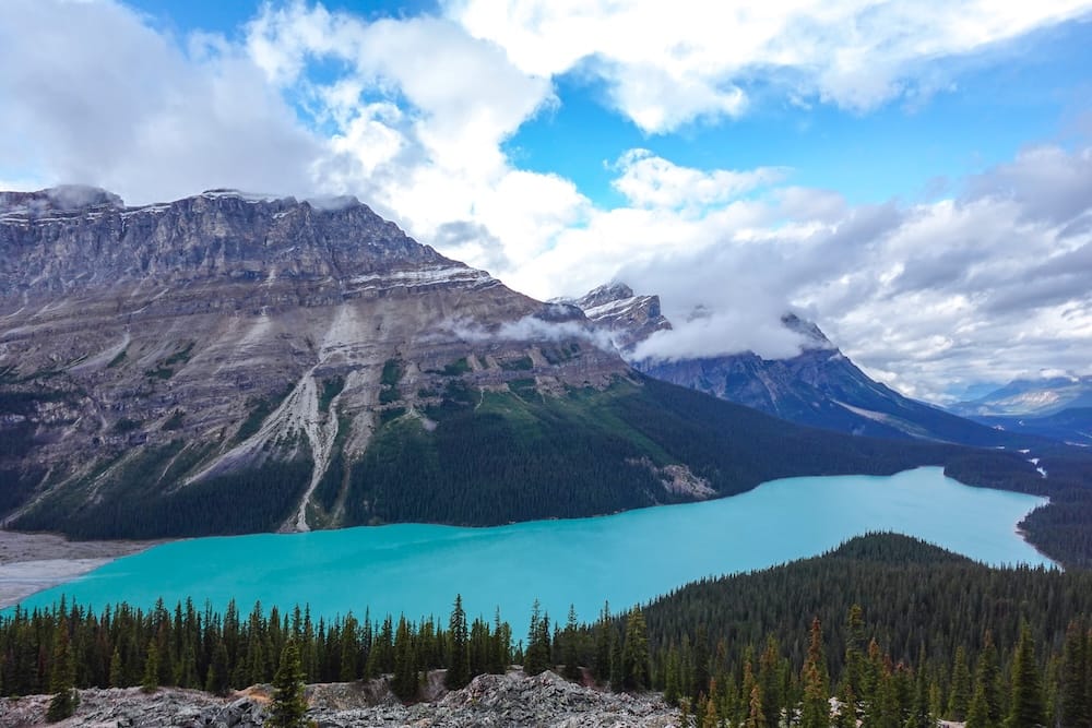 Lago Peyto desde el mirador de Bow Summit, Icefields Parkway — Parque Nacional Banff, Alberta Vista elevada del agua color turquesa intenso del lago Peyto desde el mirador de Bow Summit, rodeado de laderas boscosas y picos de montañas bajo un cielo parcialmente nublado, Parque Nacional Banff, Alberta, Canadá.