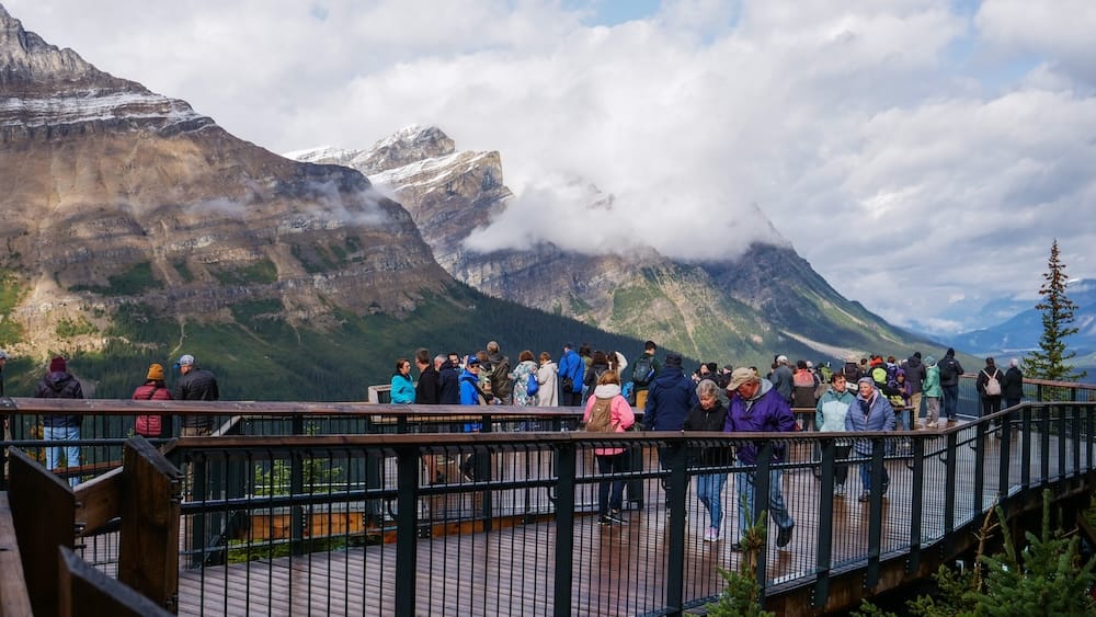 Boardwalk panorama at Peyto Lake viewpoint, Bow Summit, Icefields Parkway, Banff National Park Visitors walk along the elevated boardwalk at the Peyto Lake viewpoint on Bow Summit in Banff National Park, Alberta, with a wide panorama of cloud-draped peaks along the Icefields Parkway behind them.