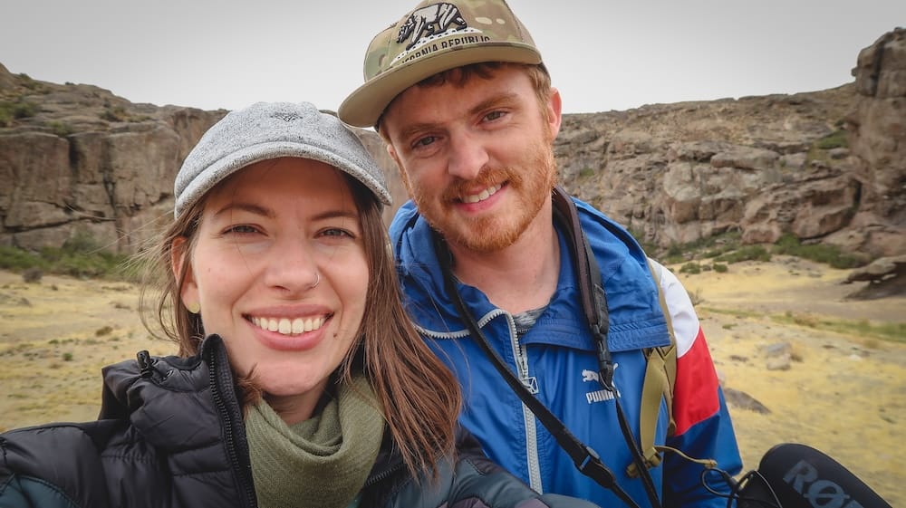 Piedra Parada canyon hike with Samuel Jeffery and Audrey Bergner in Chubut, Patagonia, Argentina landscape Samuel Jeffery and Audrey Bergner smile for a hiking selfie in front of the rocky cliffs and dry volcanic terrain of Piedra Parada in Chubut, Patagonia, Argentina.