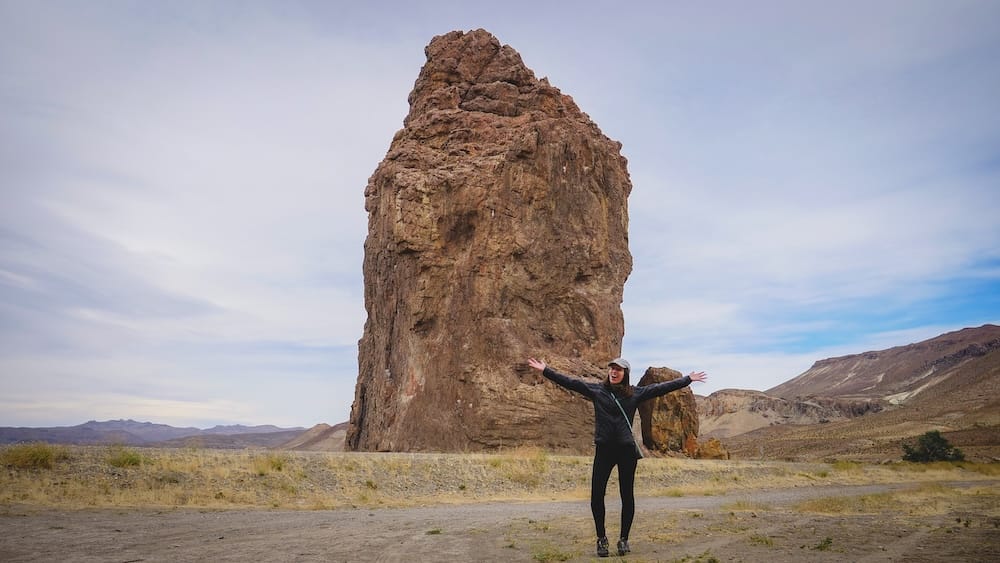 Audrey Bergner standing beside Piedra Parada in Chubut Patagonia, an exposed rock formation rising from open steppe where powerful winds sweep unobstructed, highlighting how isolated landmarks offer no protection from Patagonia’s relentless gusts.
