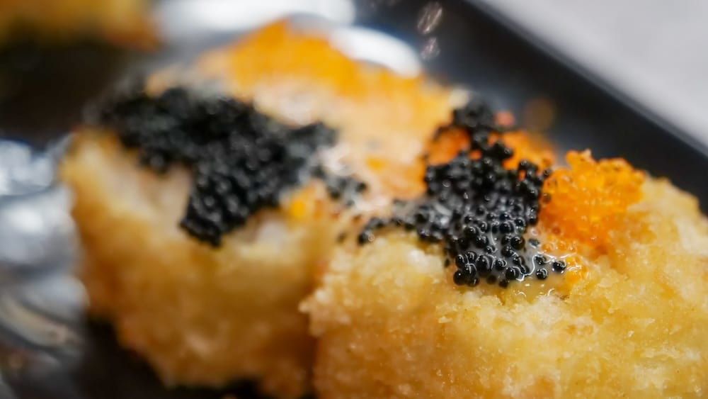 Macro close-up of sushi rolls at Point Sushi in Calgary, Alberta, Canada, with crisp golden exteriors topped by black and orange roe during the city’s creative Japanese food stop.