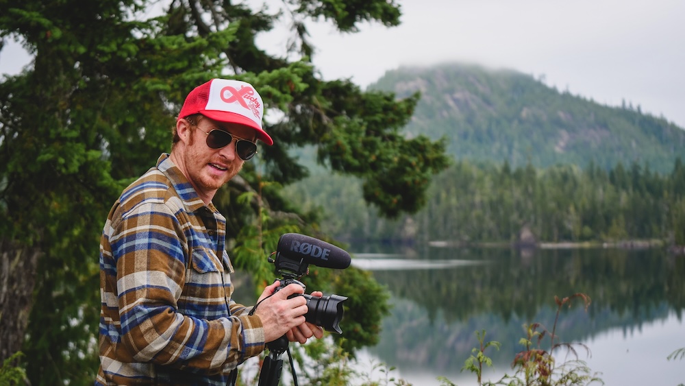 Nomadic Samuel Filming and Capturing Original Travel Photography in Port Hardy, British Columbia Port Hardy, British Columbia — Nomadic Samuel filming and photographing a calm forest lake with professional camera and microphone, capturing original travel visuals and behind-the-scenes content for Nomadic Samuel guides, videos, and licensing use.
