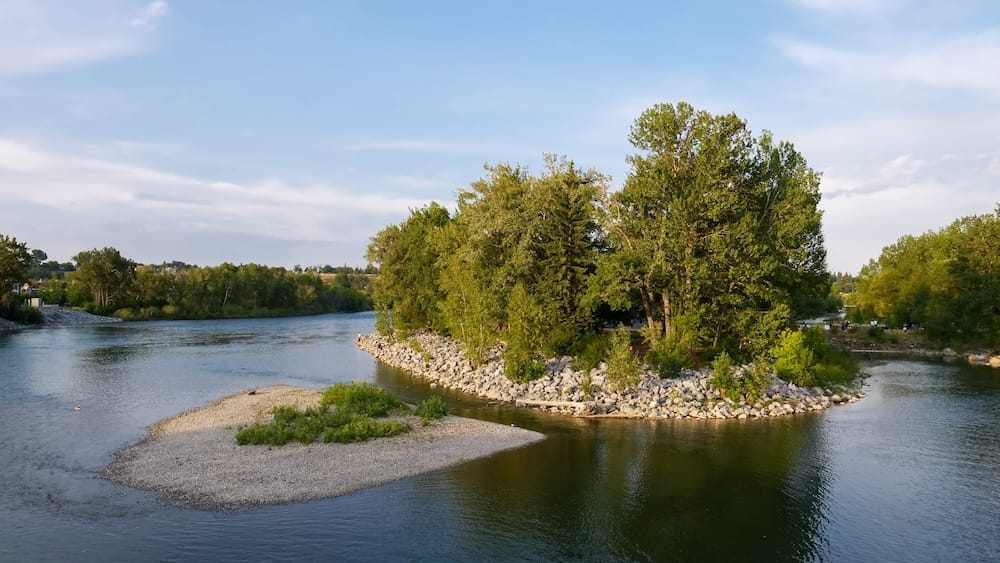Prince's Island Park, Bow River, downtown Calgary, Alberta, Canada A tree-covered island in the Bow River at Prince's Island Park, with gravel banks and people gathered under the trees on a clear evening in downtown Calgary, Alberta, Canada.