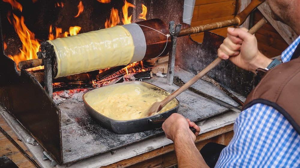 Pruegeltorte Tyrolean Cake Cooking Demonstration stands out as a cylindrical Tyrolean cake baked on a rotating spit with a fire burning in the back in Tyrol, Austria