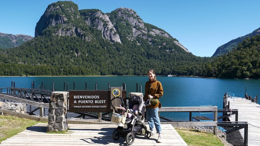 Audrey Bergner and Aurelia Jeffery at Puerto Blest in Nahuel Huapi National Park, Patagonia, Argentina Audrey Bergner stands beside Aurelia Jeffery in a stroller at Puerto Blest pier in Nahuel Huapi National Park, Río Negro, Patagonia, Argentina, with turquoise water, forested slopes and steep mountains behind them.