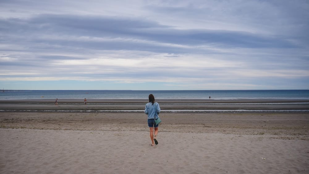 Audrey Bergner walking along the wide sandy shoreline in Puerto Madryn, Patagonia, facing the Atlantic Ocean where Welsh settlers first arrived, capturing the vast coastal landscape that shaped early migration and survival in southern Argentina.