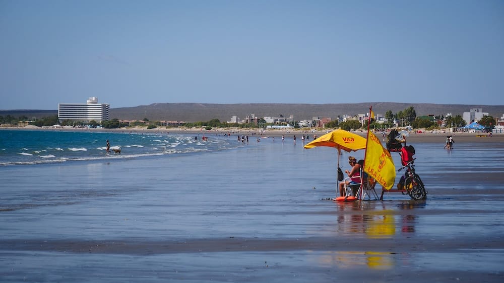 Puerto Madryn beach along the Atlantic coast in Chubut Patagonia Argentina with people relaxing by the water showing the seaside landscape typical of coastal Patagonia compared with the mountain lakes and forests of the Andes region.