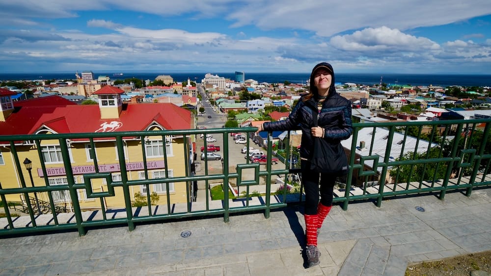 Punta Arenas Waterfront Overlook — Magallanes, Chilean Patagonia, Chile | City View with Audrey Bergner Audrey Bergner stands at a scenic overlook above the colorful waterfront of Punta Arenas, Magallanes, in Chilean Patagonia, with the Strait of Magellan and city rooftops spread below.