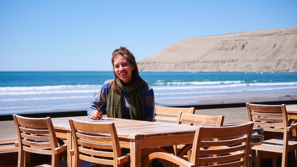 Audrey Bergner enjoying Patagonian wine overlooking Rada Tilly beach and coastal cliffs Rada Tilly beach and dramatic Patagonian coastal cliffs in Chubut Argentina where Audrey Bergner enjoys a glass of wine at an oceanfront restaurant overlooking the wide Atlantic shoreline and expansive low tide beach.