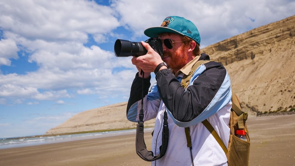 Photographer shooting along the exposed coastline of Rada Tilly in Argentine Patagonia where strong coastal winds, shifting light, and high UV conditions shape the real experience of summer travel beyond calm-looking beach scenes.