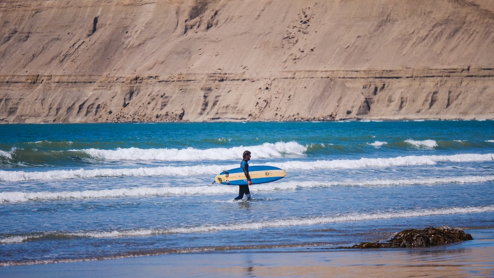 Surfer entering the waves at Rada Tilly beach in Patagonia Argentina Surfer walking into the waves at Rada Tilly on the Atlantic coast of Patagonia in Chubut Argentina where long sandy beaches and steady winds create a surprisingly good surf destination along this remote Patagonian shoreline.