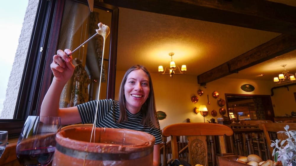 Audrey Bergner Enjoying Traditional Cheese Fondue at Restaurante Patagonia, Llao Llao Hotel, Bariloche, Patagonia Audrey Bergner lifts a cheese-covered fondue fork while dining at Restaurante Patagonia inside Llao Llao Hotel in Bariloche, Río Negro, Patagonia, Argentina, with a clay fondue pot, red wine and warm lodge-style interiors around her.
