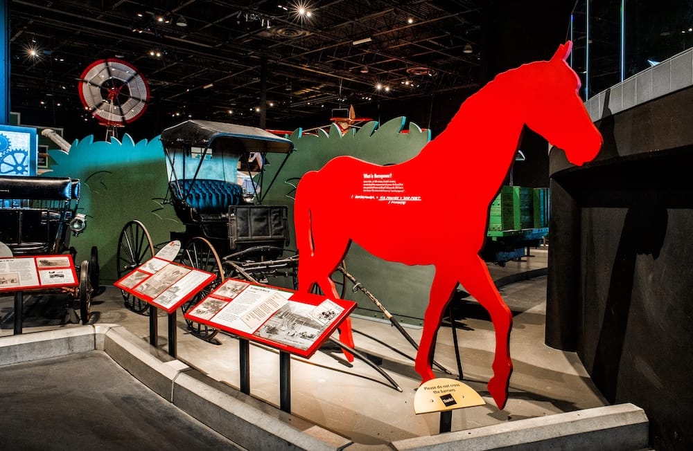 Transportation exhibits inside the Reynolds Museum in Wetaskiwin, Alberta, Canada, with historic vehicles, interpretive panels and a large red horse display under museum lighting.