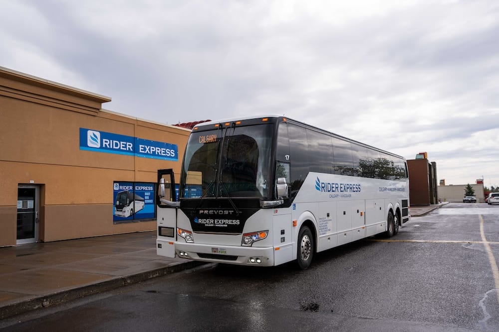 Un micro interurbano de Rider Express estacionado frente a su terminal de Calgary, Alberta, Canadá, con Calgary en el cartel del vehículo y señalización de Rider Express en el edificio.