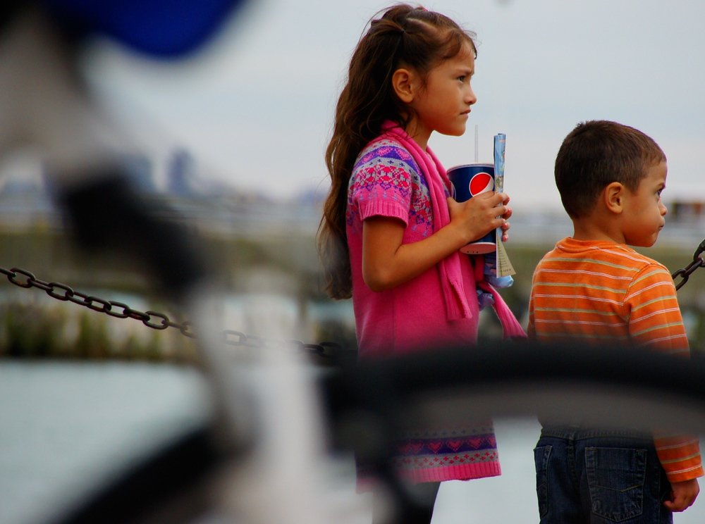 Riding a bicycle in Chicago with motion blur as a small child stands still while drinking Pepsi