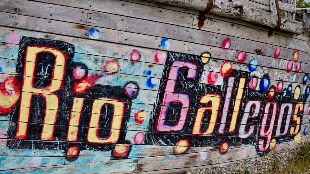 A colorful hand-painted sign spelling "Rio Gallegos" in bright red, yellow, and pink lettering decorates a weathered wooden wall in Río Gallegos, Santa Cruz, in southern Argentine Patagonia.