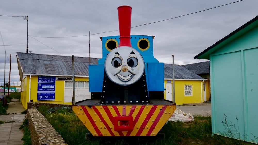 Thomas the Tank Engine Locomotive at the Railway Museum in Río Gallegos, Santa Cruz, Patagonia, Argentina A weathered Thomas the Tank Engine-style locomotive stands outside the railway museum in Río Gallegos, Santa Cruz, with brightly painted buildings beneath an overcast Patagonian sky in Argentina.