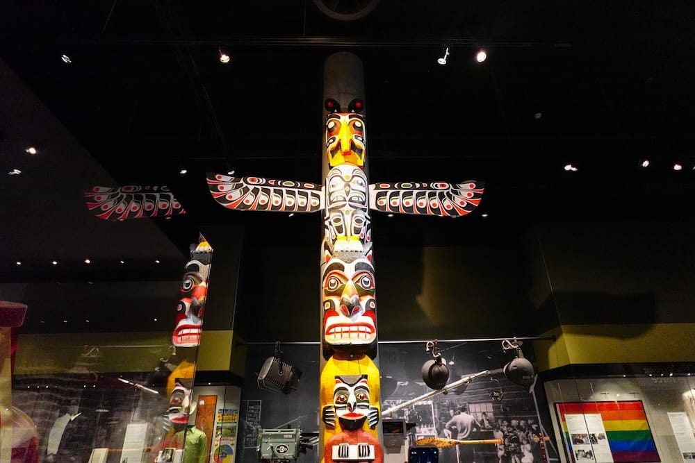 Indigenous Carved Poles in the Royal Alberta Museum Cultural Gallery, Edmonton, Alberta, Canada Tall painted Indigenous carved poles displayed beneath gallery lighting inside the Royal Alberta Museum in Edmonton, Alberta, Canada, with exhibit panels and historic photographs surrounding them.
