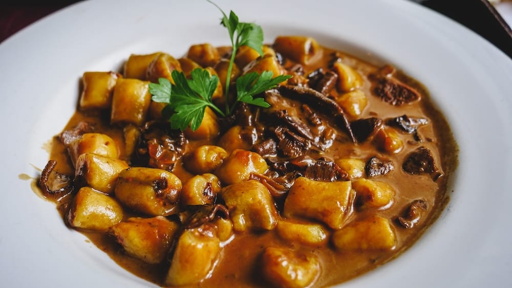 Rustic ñoquis served with wild mushrooms and a rich meat ragù in Trelew, Chubut, Patagonia, Argentina, finished with fresh parsley in a wide white bowl.