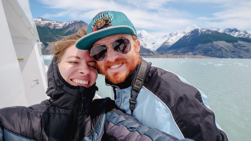 Samuel y Audrey en el crucero por el Lago Argentino cerca del Perito Moreno, El Calafate, Santa Cruz, Argentina Samuel Jeffery y Audrey Bergner sonriendo juntos en la cubierta de un barco de crucero por el Lago Argentino, con el pelo despeinado por el viento y anteojos de sol, rodeados de témpanos, agua glaciar turquesa y picos andinos nevados cerca del Glaciar Perito Moreno, El Calafate, Santa Cruz, Patagonia argentina.
