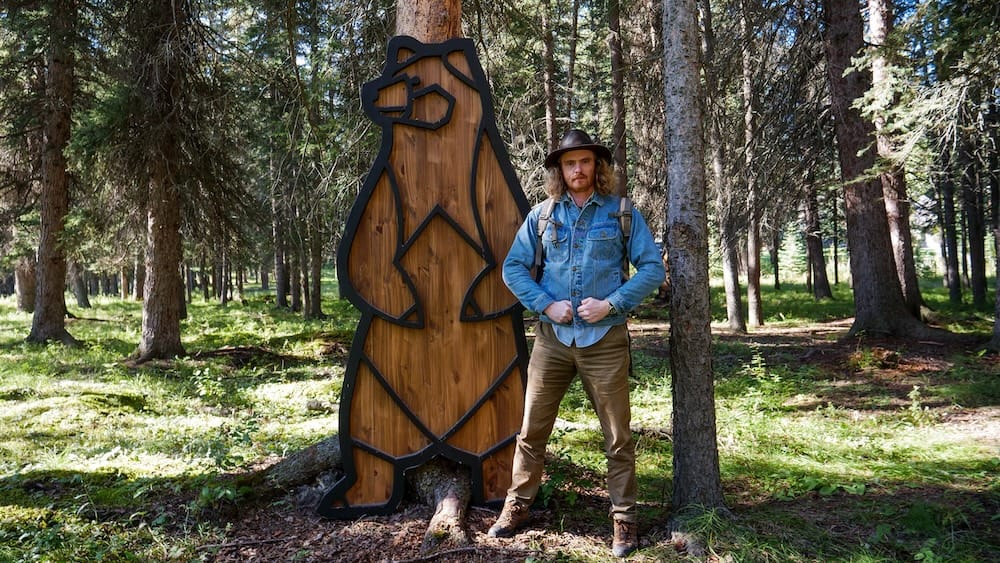 Bear sculpture installation on the Art in Nature Trail, Banff, Alberta, Canada Samuel Jeffery stands beside a life-size wooden bear sculpture among the trees on the Art in Nature Trail in Banff, Alberta, Canada, one of the exhibition's installations along the Bow River corridor.