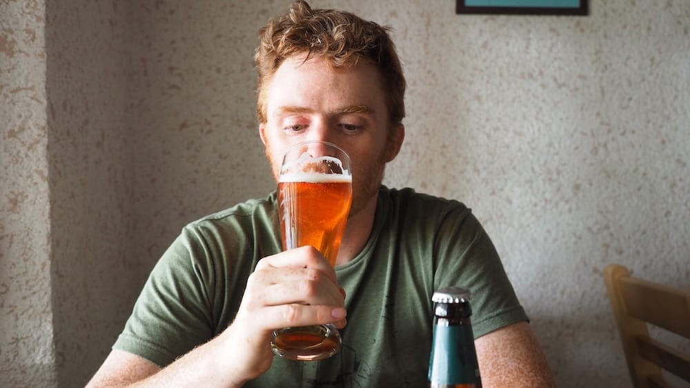 Samuel Jeffery holds a tall glass of amber beer while seated at Fat Cat Cafe in Karakol, Kyrgyzstan, capturing a relaxed break from traditional dishes during our wider food trip across the country.
