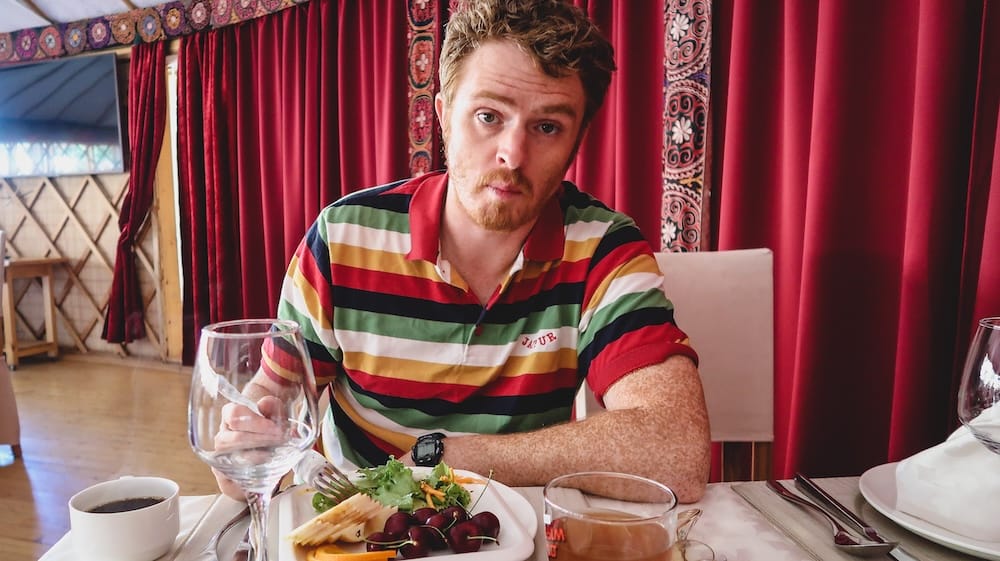 Samuel Jeffery sits at a restaurant table in Kyrgyzstan with a plate of fresh salad, sliced vegetables and dark red cherries, offering a lighter contrast to the country’s rich meat, noodle and dumpling dishes.
