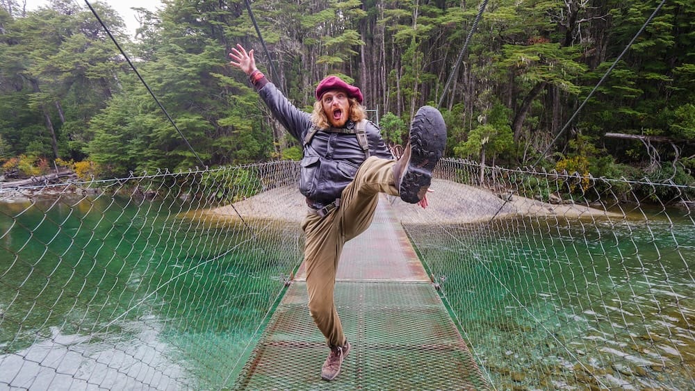 Samuel Jeffery mid-jump on a suspension bridge in El Bolsón wearing casual gear, illustrating a common Patagonia travel mistake of underestimating terrain and conditions where proper footwear and caution are essential
