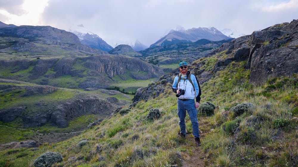 Samuel Jeffery Exploring the Glacial Peaks of El Chaltén in Argentine Patagonia Samuel Jeffery stands with his camera on a rocky hiking trail beneath dramatic glacial peaks near El Chaltén in Santa Cruz, Argentine Patagonia.