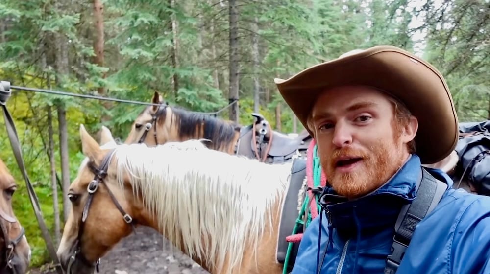 Samuel Jeffery y Hollywood, descanso en el sendero, Banff Trail Riders, Parque Nacional Banff, Alberta, Canadá Samuel Jeffery hace una pausa junto a su caballo Hollywood, atado entre otros caballos en el bosque, durante un descanso en una excursión a caballo por el interior con Banff Trail Riders en el Parque Nacional Banff, Alberta, Canadá.