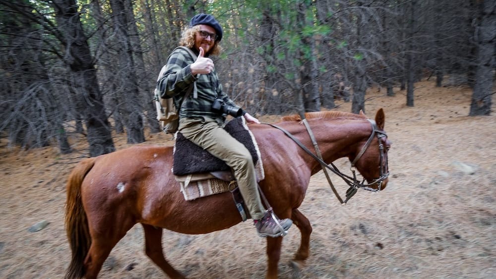 Samuel Jeffery gives a thumbs up while riding a horse through a pine forest at Estancia Arroyo Verde in Neuquén, Argentine Patagonia, during a guided horse trek on the property.