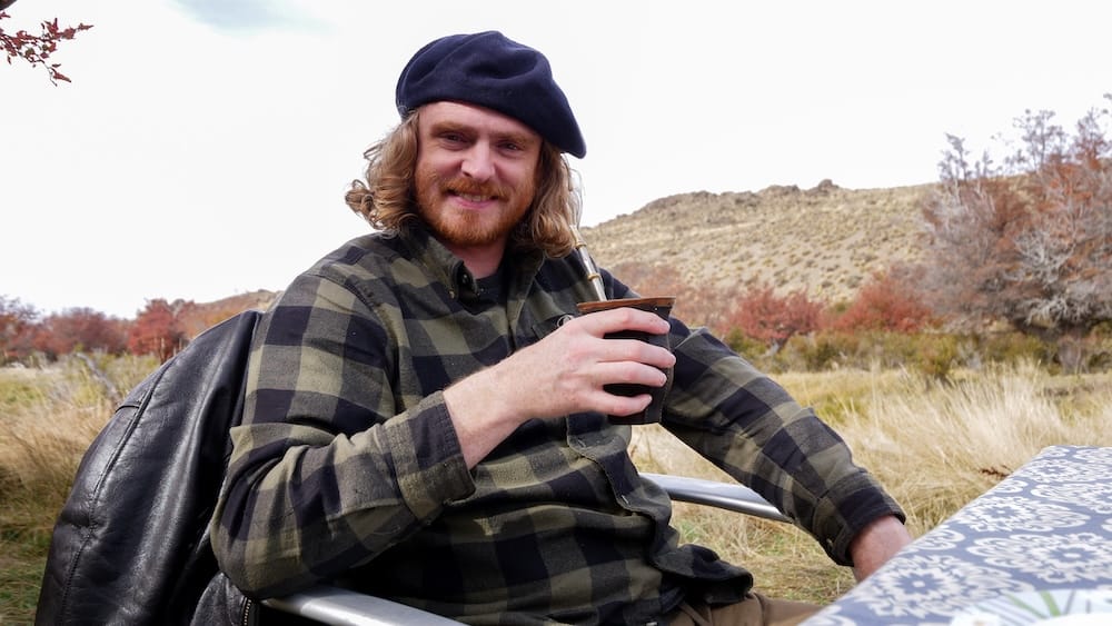 Samuel Jeffery drinking mate at Estancia Tecka Lodge in Patagonia, holding a traditional gourd and metal straw in a rugged landscape, reflecting Argentina’s everyday tea ritual that balances the region’s rich dessert culture
