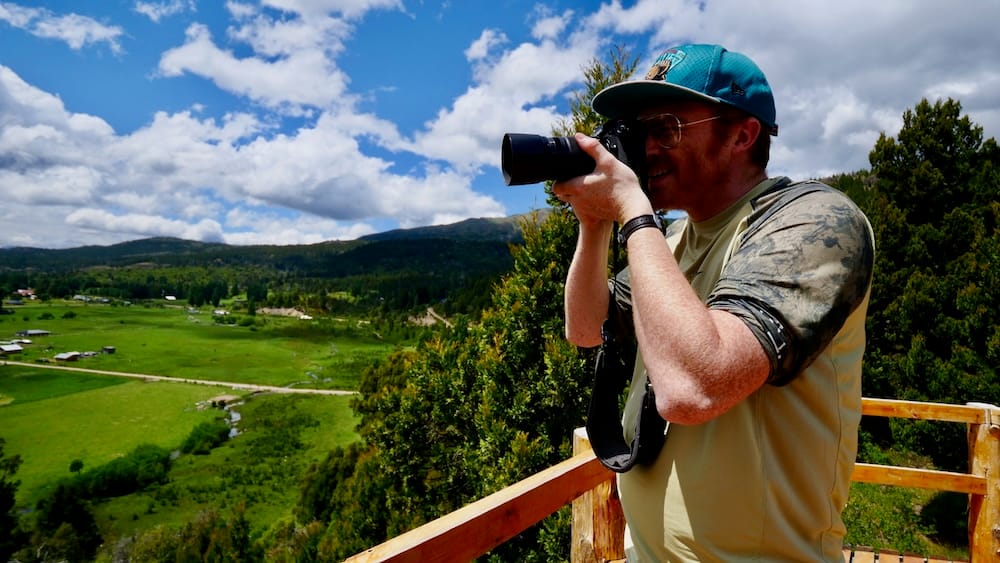 Samuel Jeffery Fotografiando el Valle de El Bolsón en la Patagonia Argentina El Bolsón turismo: Samuel Jeffery fotografía el valle de la Comarca Andina desde un mirador de madera, cuidando la lente de los vientos patagónicos.