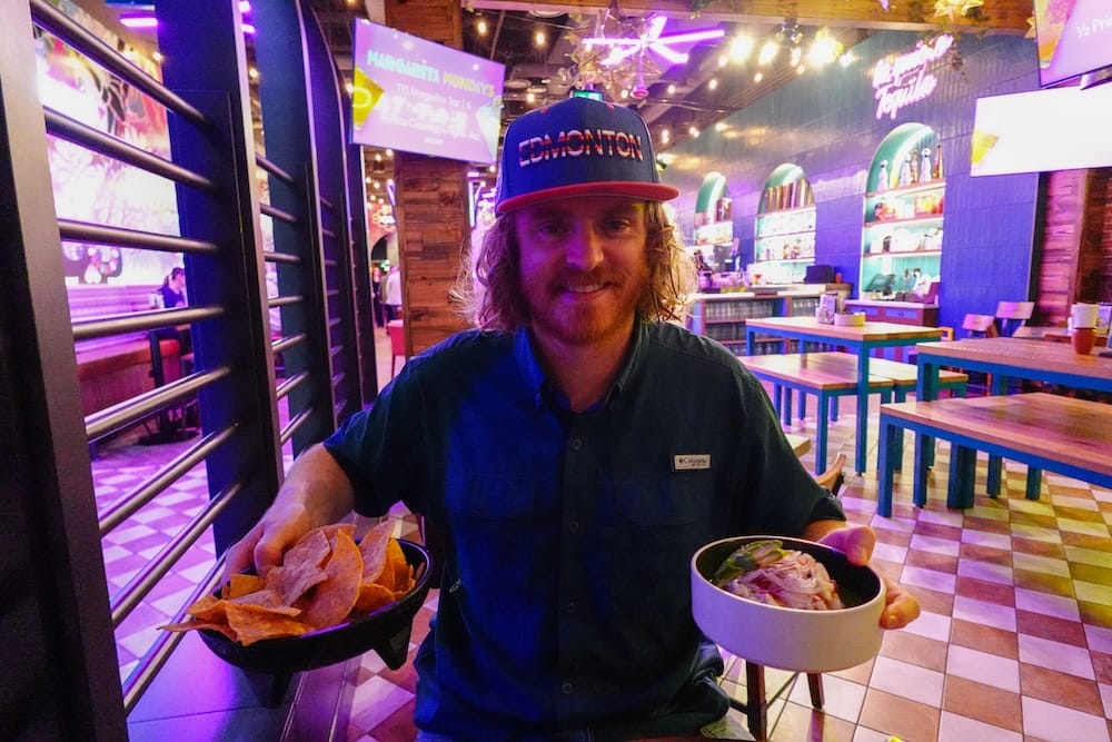 Samuel Jeffery sostiene un bowl de nachos y un plato de ceviche en The Taco Shop, sobre Bourbon Street, dentro del West Edmonton Mall, Edmonton, Alberta, Canadá.