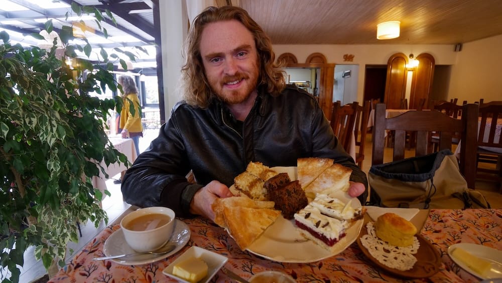 Samuel Jeffery Welsh tea Trevelin Patagonia Nain Maggie tea house cakes and scones experience Argentina Samuel Jeffery enjoying a traditional Welsh tea service at Casa de Té Nain Maggie in Trevelin Patagonia Argentina, featuring cakes, scones, and tea inside a cozy Andean tea house setting that reflects the region’s rich cultural heritage