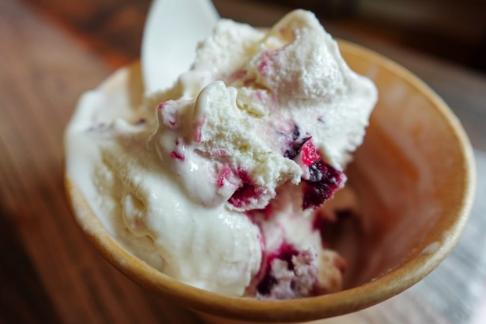 A close-up bowl of Saskatoon Berry ice cream, vanilla with dark purple berry swirls, from Harvey's Confectionery at Heritage Park in Calgary, Alberta, Canada.