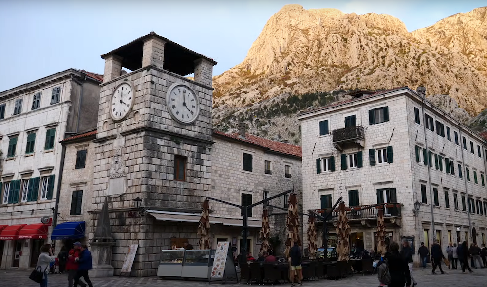 Seagate clock tower with mountain backdrop and pedestrians in Kotor, Montenegro 