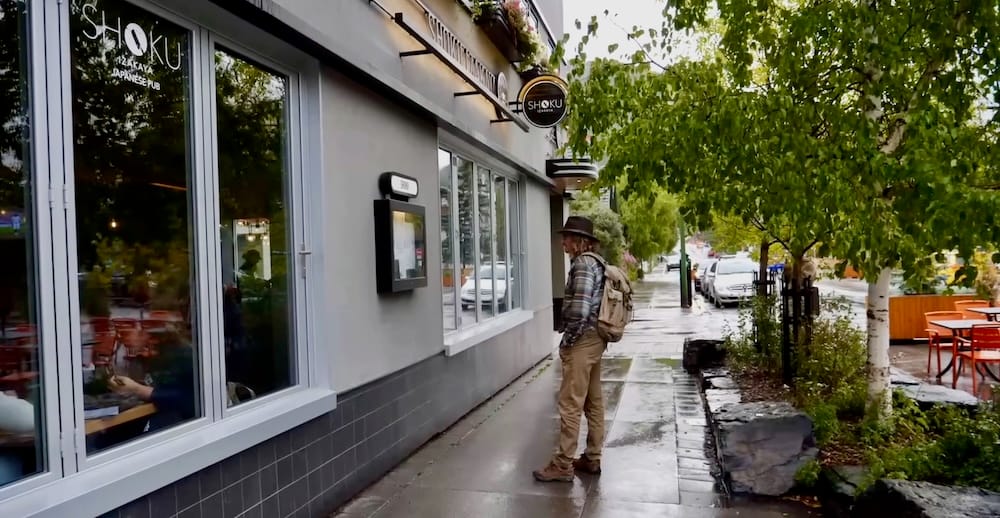 Samuel Jeffery outside Shoku Izakaya, Caribou Street, Banff, Alberta Samuel Jeffery stands on the sidewalk outside Shoku Izakaya Japanese Pub on Caribou Street in Banff, Alberta, Canada, with the restaurant's storefront and window seating visible beside him.