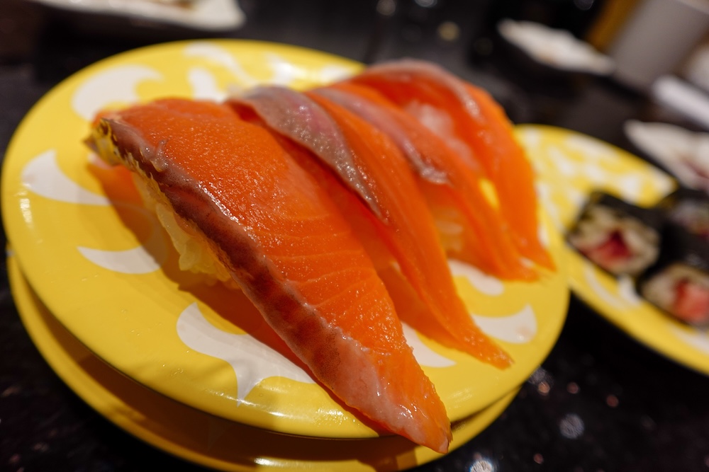 Nigiri de salmón servido en un plato amarillo de Kaiten Sushi Hakodate Shunka, restaurante de cinta transportadora en Hokkaido, Japón Primer plano de varias piezas de nigiri de salmón, con gruesas láminas anaranjadas de pescado crudo sobre arroz, servidas en un plato amarillo del restaurante de sushi con cinta transportadora Shunka, en Hakodate, Hokkaido, Japón.
