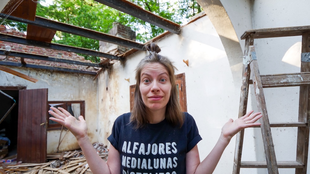 Sierras de Córdoba, Argentina renovation project scene, with Audrey Bergner standing inside a partially demolished family property, smiling with raised hands as we begin restoring a neglected house in the mountains.