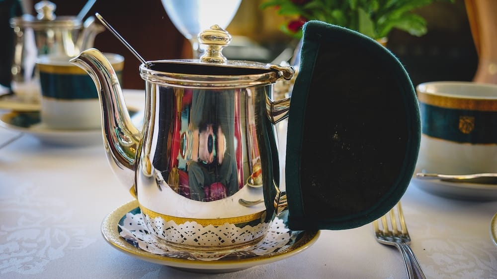 Silver Teapot Set for Afternoon Tea at Llao Llao Hotel, Bariloche, Río Negro, Argentine Patagonia A polished silver teapot with a spoon resting inside sits on a lace doily and gold-rimmed saucer beside a folded green napkin during afternoon tea service at Llao Llao Hotel in Bariloche, Río Negro, Argentine Patagonia, Argentina.