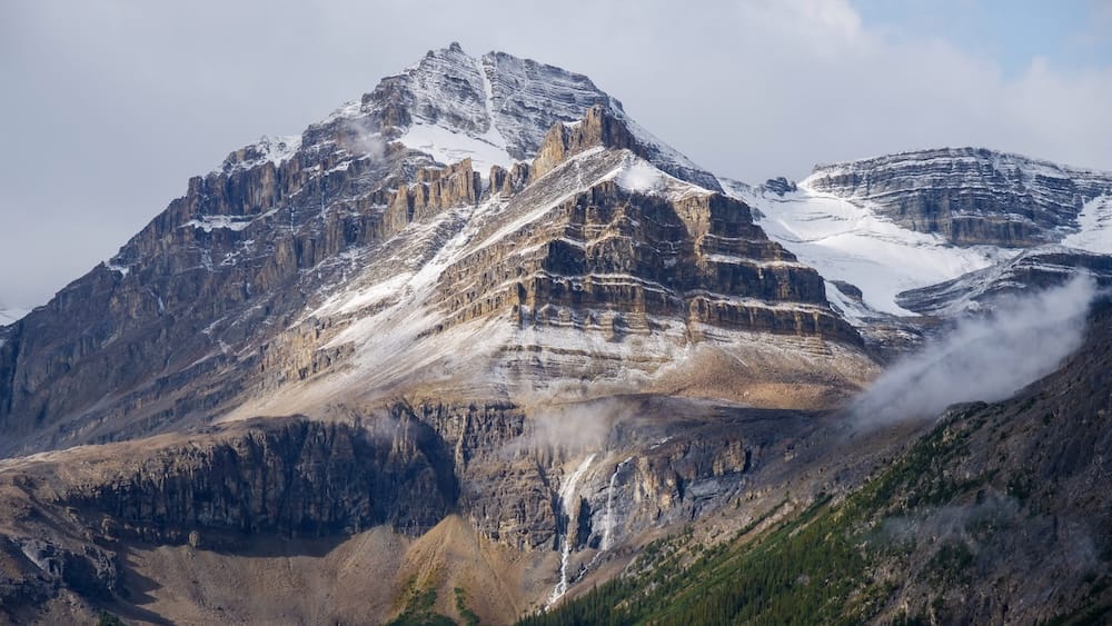 Snow-capped peak near Bow Summit, Icefields Parkway, Banff National Park, Alberta A rugged, snow-streaked peak rises above the Icefields Parkway near Bow Summit in Banff National Park, Alberta, with thin meltwater streams visible cutting down the exposed rock face.