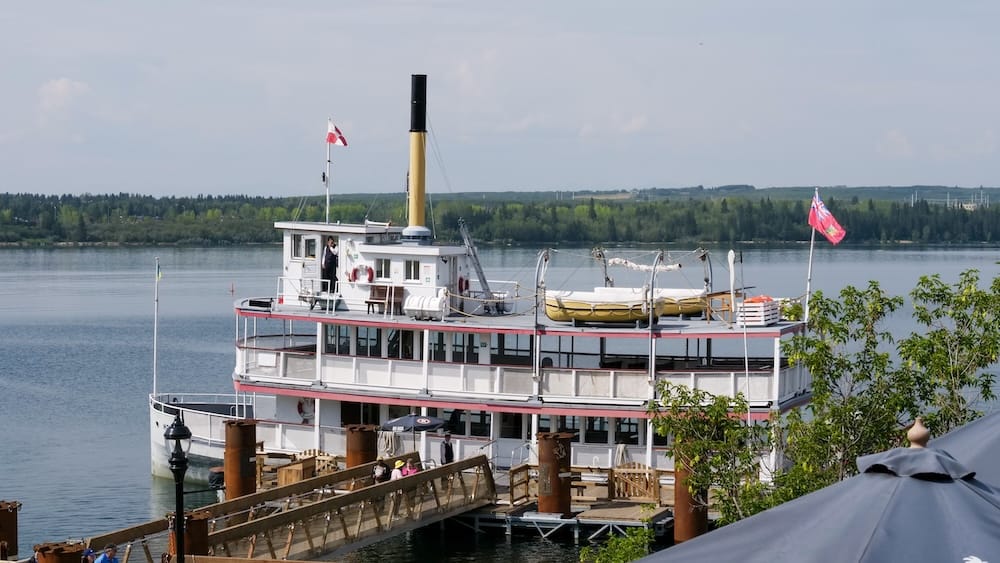 S.S. Moyie paddlewheeler docked on the Glenmore Reservoir, Heritage Park, Calgary, Alberta, Canada The S.S. Moyie paddlewheeler sits docked at Heritage Park's pier on the Glenmore Reservoir in Calgary, Alberta, Canada, with its smokestack, upper deck seating, and a red ensign flag visible against the water and tree-lined shore.