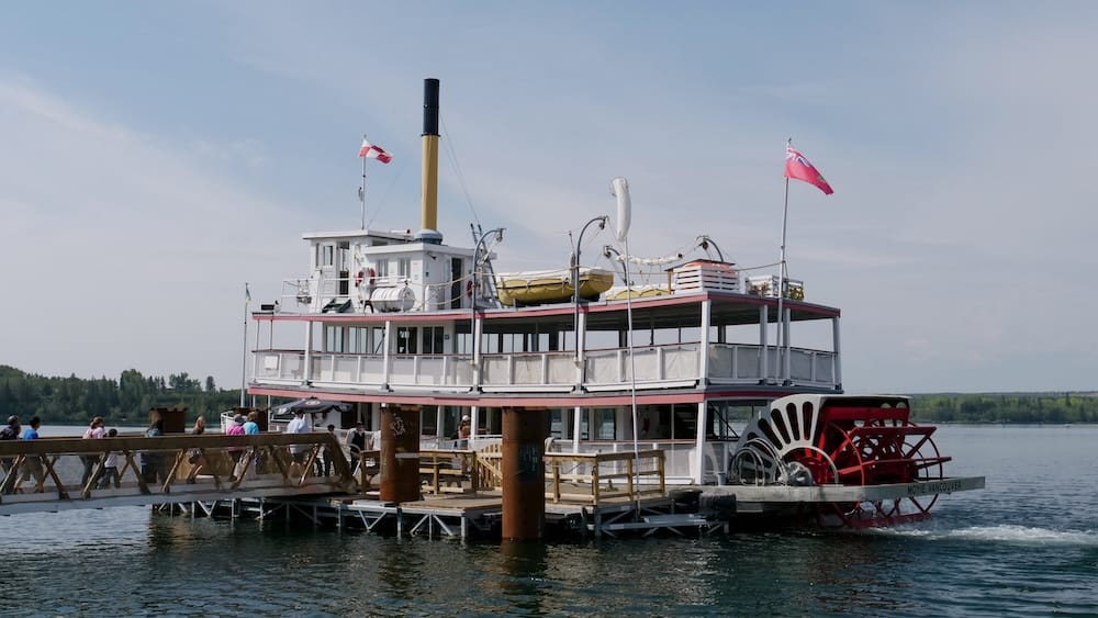 The S.S. Moyie paddlewheeler docked at Heritage Park Historical Village in Calgary, Alberta, Canada, with passengers boarding along the wooden pier on the Glenmore Reservoir.