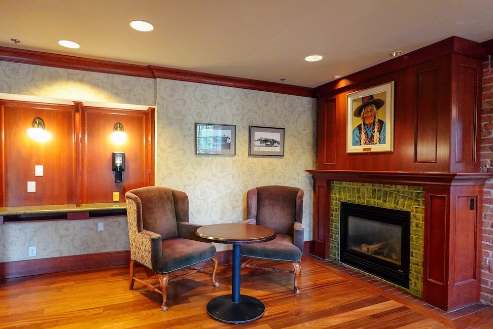 St. Eugene Golf Resort & Casino in Cranbrook, British Columbia, showing a cozy fireplace seating area inside the Mission Building, with wood floors, upholstered chairs, and warm lighting that creates a relaxed, inviting space for guests to unwind.